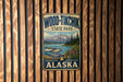A vintage-style metal sign for Wood-Tikik State Park in Alaska, featuring a scenic image of a lake, mountains, and a plane.