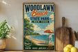 A vintage-style sign for Woodlawn Beach State Park in New York, featuring a beach scene with a lifeguard chair, umbrella, and a wooden paddle.