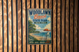 A vintage-style metal sign for Woodlawn Beach State Park in New York, featuring a beach scene with a lifeguard chair and an umbrella.