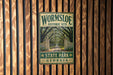 A metal sign for Wormsloe Historic Site in Georgia, featuring a path lined with trees and a gate, mounted on a wooden wall.