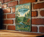 A vintage-style metal sign for Wrentham State Forest, featuring a scenic illustration of a forest landscape with a river and mountains in the background.