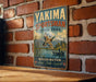 A vintage-style metal sign for Yakima Sportsman State Park, featuring a scenic illustration of ducks and a mountain backdrop, mounted on a brick wall.