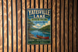 A vintage-style metal sign for Yatesville Lake State Park in Kentucky, featuring a scenic image of a lake with a canoe and mountains in the background.