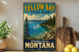 A vintage-style sign for Yellow Bay State Park in Montana, featuring a scenic landscape with pine trees, mountains, and a lake.