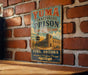 A vintage-style metal sign for Yuma Territorial Prison, featuring a brick wall and a desert landscape illustration, is displayed on a wooden surface.