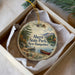 A decorative ornament in a box, featuring a scenic image of a lake, mountains, and a boat, with the text "Ahern State Park, New Hampshire" printed on it.