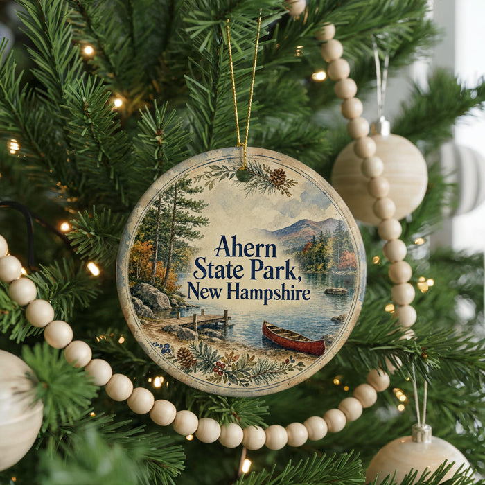 A round ornament hanging on a Christmas tree, featuring a scenic image of a lake and mountains with a boat in the water.