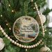 A round ornament hanging on a Christmas tree, featuring a scenic image of a lake and mountains with a boat in the water.