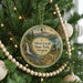 A round ornament hanging on a Christmas tree, featuring a scenic landscape with a waterfall and mountains.