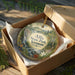 A decorative ornament in a box, featuring a scenic landscape with a waterfall and forest.