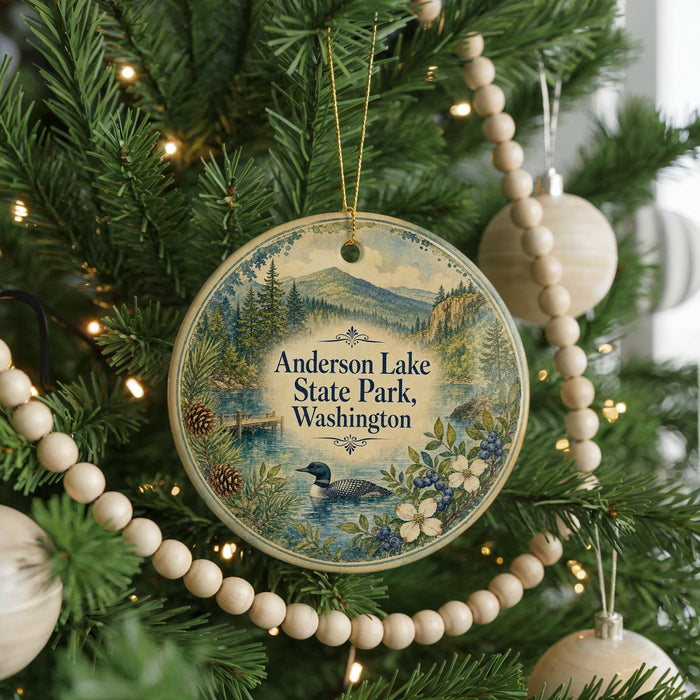 A round ornament hanging on a Christmas tree, featuring a scenic landscape with a lake and mountains.