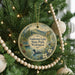 A round ornament hanging on a Christmas tree, featuring a scenic landscape with a lake and mountains.