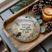 A decorative ornament featuring a bison and a deer, with the text "Antelope Island State Park, Utah" on it, placed on a wooden tray alongside pine cones and a lit candle.