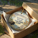 A decorative ornament in a box, featuring an illustration of a bison and a deer in a scenic landscape, with the text "Antelope Island State Park, Utah" printed on it.