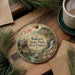 A decorative ornament featuring a scenic landscape with a waterfall, pine trees, and a house, hanging on a wooden surface.