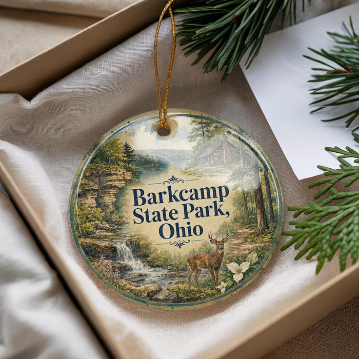 A decorative ornament with a scenic landscape featuring a waterfall, pine trees, and a deer, hanging from a string.