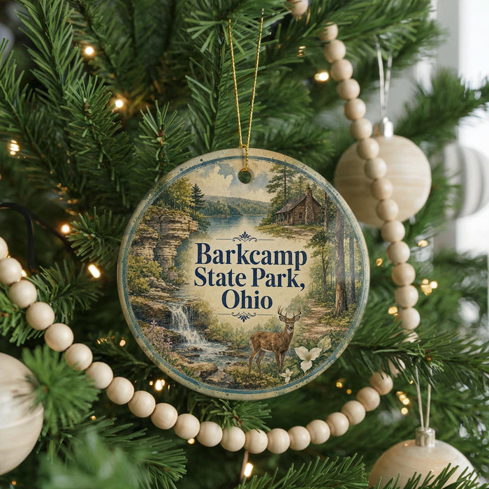 A round ornament hanging on a Christmas tree, featuring a scenic landscape with a waterfall and a cabin in the background.