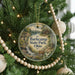 A round ornament hanging on a Christmas tree, featuring a scenic landscape with a waterfall and a cabin in the background.