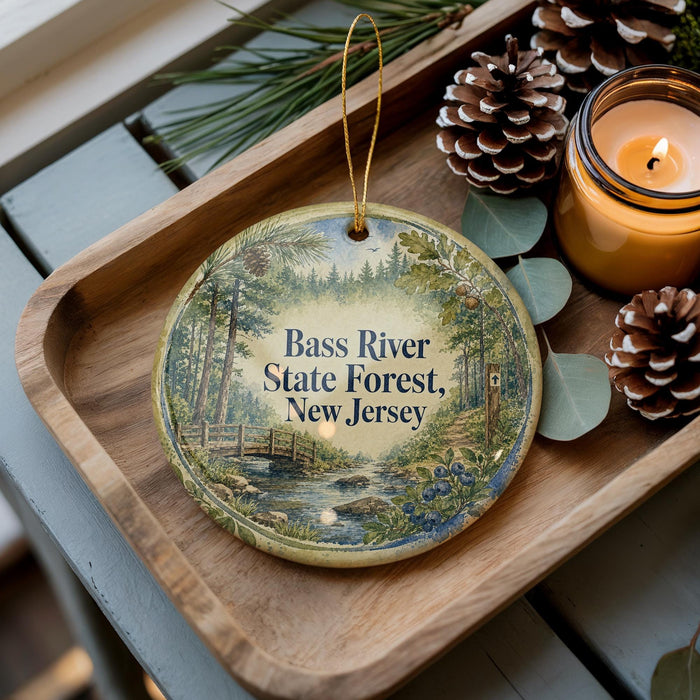 A wooden tray with a decorative ornament featuring a scenic image of the Bass River State Forest in New Jersey, accompanied by pine cones and a lit candle.