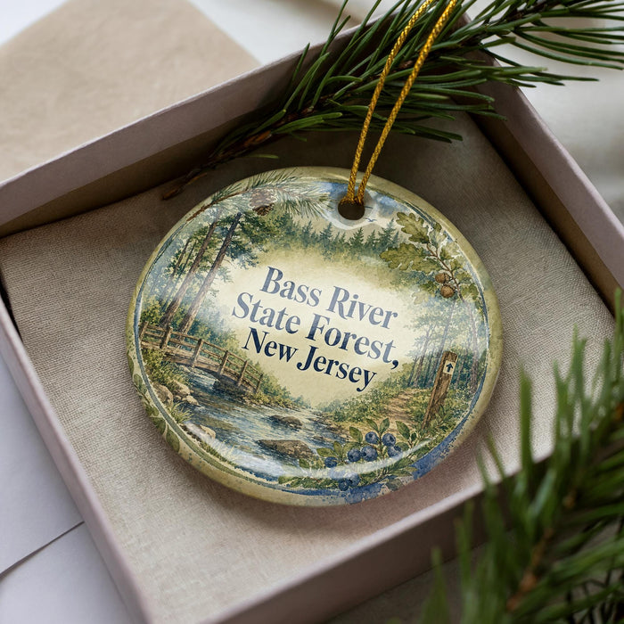 A decorative ornament with a scenic image of a river and forest, placed in a box with pine branches.