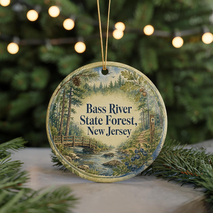 A round ornament with a painting of a forest scene hangs in front of a Christmas tree with twinkling lights.