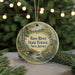 A round ornament with a painting of a forest scene hangs in front of a Christmas tree with twinkling lights.