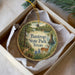A decorative ornament in a box, featuring a scenic image of Bastrop State Park, Texas, with a deer and a bridge in the background.