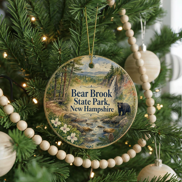 A circular ornament hanging on a Christmas tree, featuring a scenic image of Bear Brook State Park in New Hampshire.