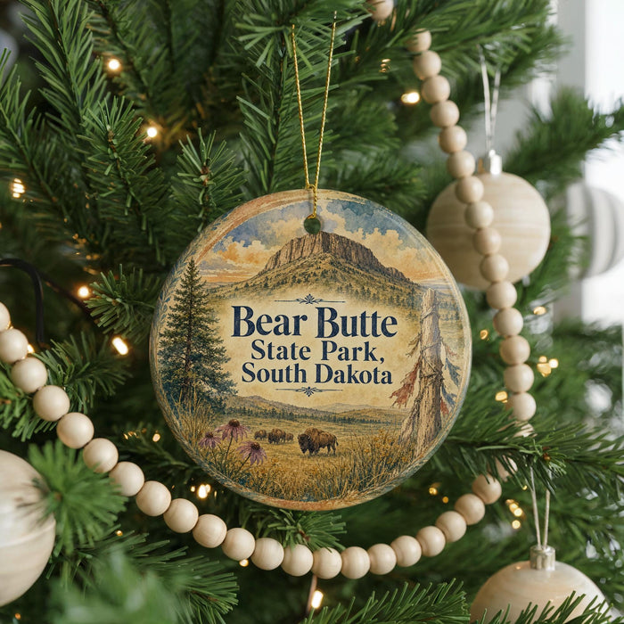 A round ornament hanging on a Christmas tree, featuring a scenic landscape with a mountain and pine trees.
