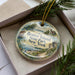 A decorative ornament in a box, featuring a scenic image of Beaver Island State Park, New York.