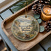 A wooden tray with a decorative ornament featuring a scenic image of Beavertail Hill State Park, Montana, and pine cones.