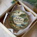 A decorative ornament in a box, featuring a scenic landscape with pine trees, a lake, and a dock, with the text "Belfair State Park, Washington" prominently displayed.