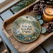 A decorative ornament featuring a scenic image of Belle Isle State Park, Virginia, with pine cones and a lit candle on a wooden tray.