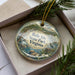 A decorative ornament in a box, featuring a scenic landscape with a bird and water, along with the text "Belle Isle State Park, Virginia".