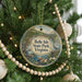 A round ornament hanging on a Christmas tree, featuring a scenic landscape with a river and trees.