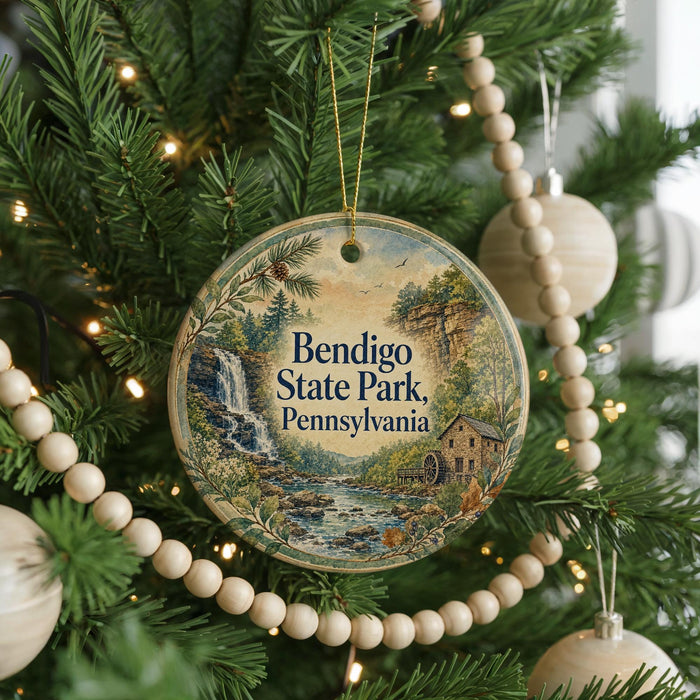 A round ornament hanging on a Christmas tree, featuring a scenic image of Bendigo State Park in Pennsylvania.