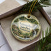 A decorative ornament in a box, featuring a scenic landscape with a waterfall and a cabin, with the text "Benjamin Rush State Park, Pennsylvania" printed on it.