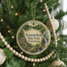 A round ornament hanging on a Christmas tree, featuring a scenic landscape with a waterfall and a cabin.