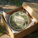 A round ornament in a box, featuring a scenic landscape of Benjamin Rush State Park in Pennsylvania.