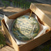 A decorative ornament in a box, featuring a scenic landscape with a waterfall and greenery.