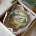 A decorative ornament in a box, featuring a scenic landscape with a beach, mountains, and a body of water.