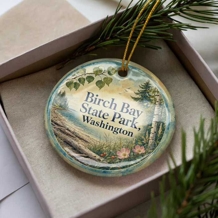 A decorative ornament in a box, featuring a scenic landscape with a body of water, trees, and flowers.