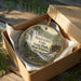 A decorative ornament in a brown box, featuring a scenic image of Blackwater Falls State Park West Virginia.