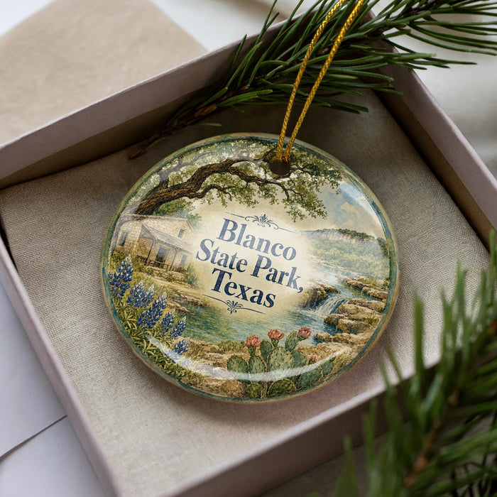 A decorative ornament in a box, featuring a scenic landscape with a house, trees, and a waterfall.