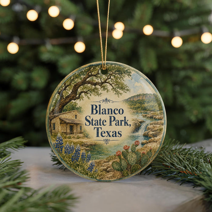 A circular ornament with a scenic landscape of Blanco State Park, Texas, featuring a house, trees, and a waterfall.