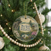 A round ornament hanging on a Christmas tree, featuring a scenic landscape with a mountain, a lake, and a bird.