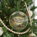 A round ornament hanging on a Christmas tree, featuring a scenic landscape with a mountain and a house, surrounded by greenery and flowers.