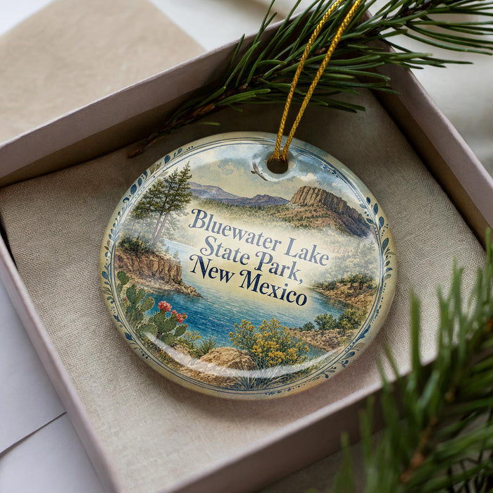 A decorative ornament in a box, featuring a scenic landscape with mountains, water, and greenery.