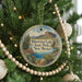 A Christmas tree ornament with a scenic image of Bluewater Lake State Park, New Mexico, surrounded by pine branches and beaded decorations.