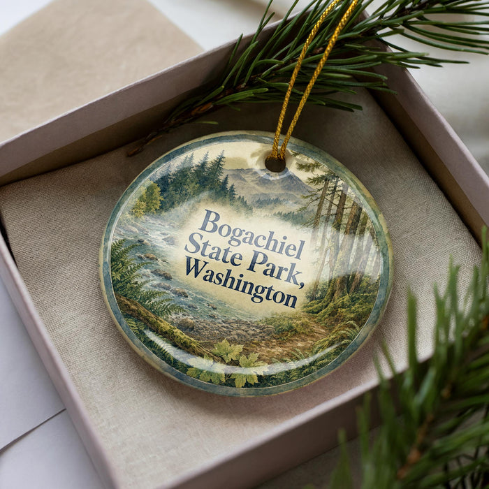 A decorative ornament in a box, featuring a scenic landscape with pine trees and mountains, with the text "Bogachiel State Park, Washington" prominently displayed.